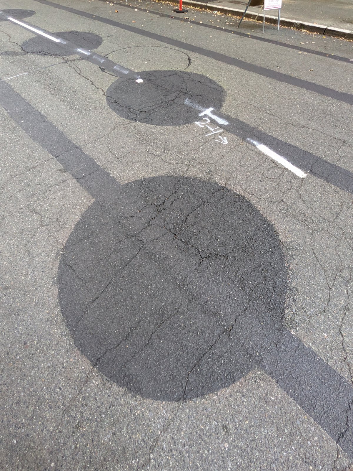 A painted-over circle on Ninth Avenue, cracked asphalt showing through the dark paint, with a chalk mark and a stripe running through it.